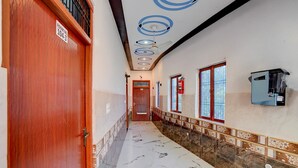 A hallway with a wooden door labeled 'ROOM NO. 104-3', a ceiling fan, a fire extinguisher, and a water dispenser. - Classic Hotel Siya Raman (Faizabad)