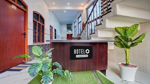 A hotel reception area with a wooden reception desk, a sign indicating it's a company-serviced hotel, and potted plants. - Classic Hotel Siya Raman (Faizabad)