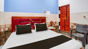 A hotel room with a large bed, a red headboard, a small table with a vase, and a wooden cabinet. - Classic Hotel Siya Raman (Faizabad)