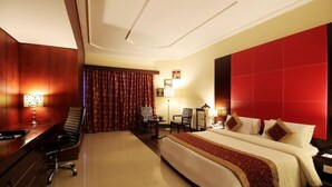 Une chambre d’hôtel avec un grand lit, un bureau, deux chaises, un mur d’accent rouge et un plafond doté d’un éclairage encastré.