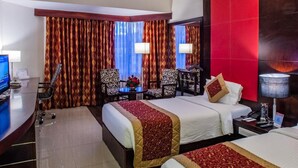 Une chambre d’hôtel avec deux lits, un bureau, une chaise, une télévision et un mur d’accent rouge.