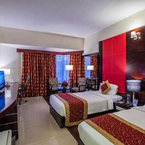 Ein Hotelzimmer mit zwei Betten, einem Schreibtisch, einem Sessel, einem Fernseher und einer Wand in Rot.