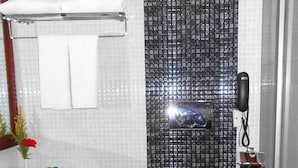 Une salle de bain avec un mur de douche recouvert de carreaux noirs, un lavabo blanc, un miroir et un téléphone.