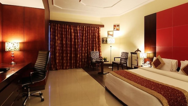 Une chambre d’hôtel avec un lit, un bureau, des chaises et une grande fenêtre avec des rideaux.
