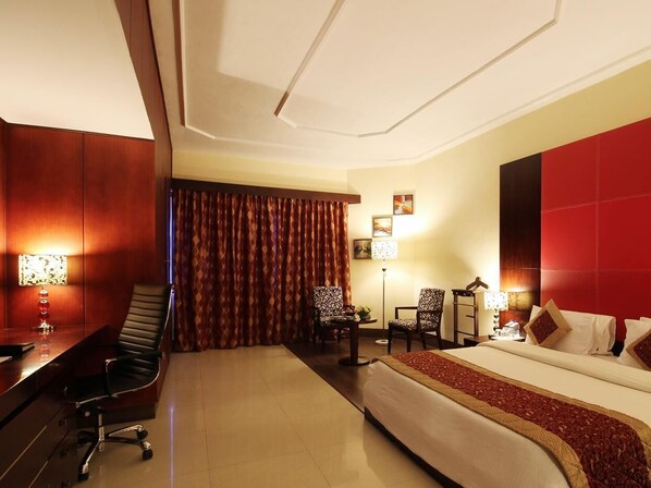 A hotel room with a bed, desk, chairs, and a large window with curtains. - Fortune Hotel South Park, Trivandrum (Thiruvananthapuram)
