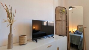Camera da letto moderna con una TV su una cassettiera bianca, uno specchio e un letto con copripiumino blu.