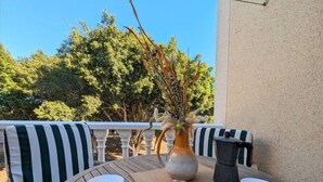 Un tavolo di legno con due tazze e piattini bianchi, un vaso con piante secche e un condimento per sale in pietra su un balcone con mobili da esterno a righe.