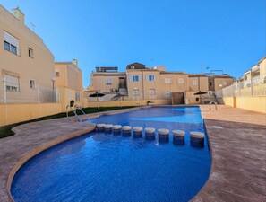 A swimming pool with a tiled deck, surrounded by buildings with balconies and windows.