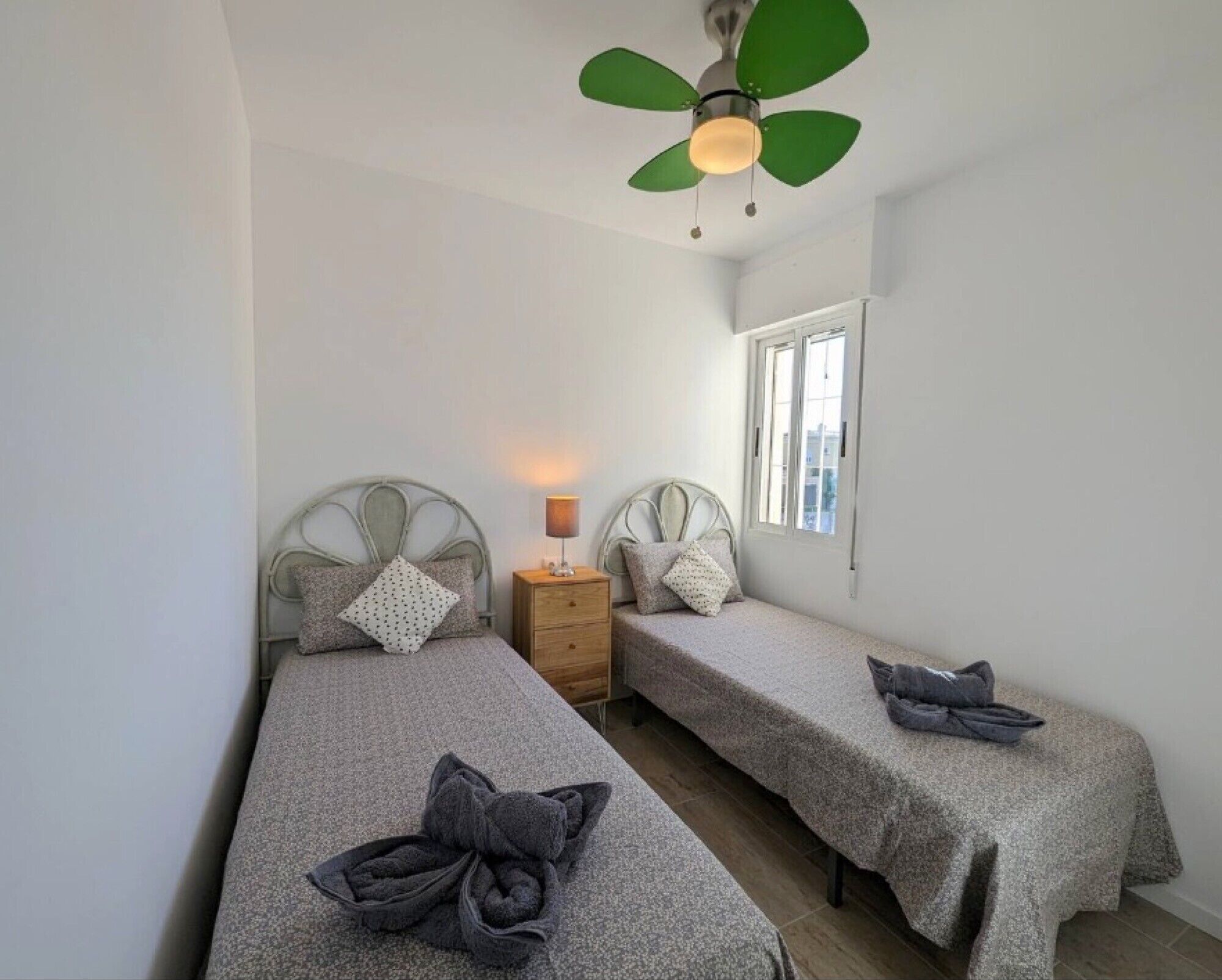 Ein Schlafzimmer mit zwei Einzelbetten, einem Nachttisch, einer Lampe, einem Deckenventilator und einem Fenster.