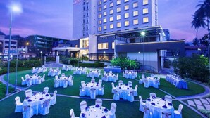 Un hotel de diseño moderno, con un amplio espacio exterior para comer con mesas y sillas redondas, y un edificio bien iluminado con un letrero visible.