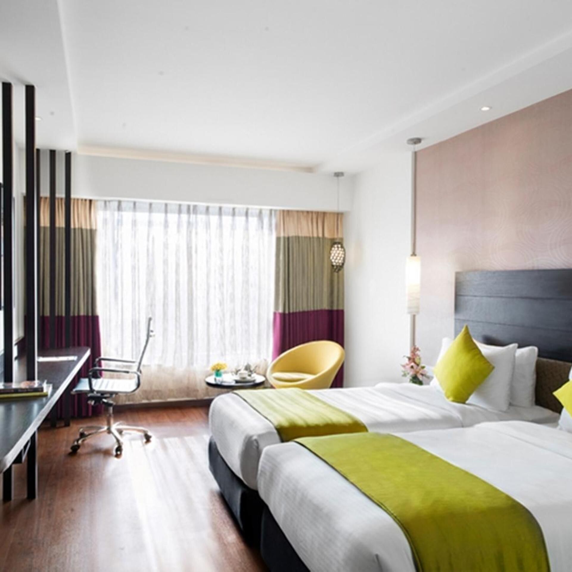 A hotel room with two beds, a desk, a chair, and a window with curtains.