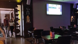 Un restaurante tenuemente iluminado con mesas y sillas, una pantalla de televisión en la pared y un revestimiento de madera.
