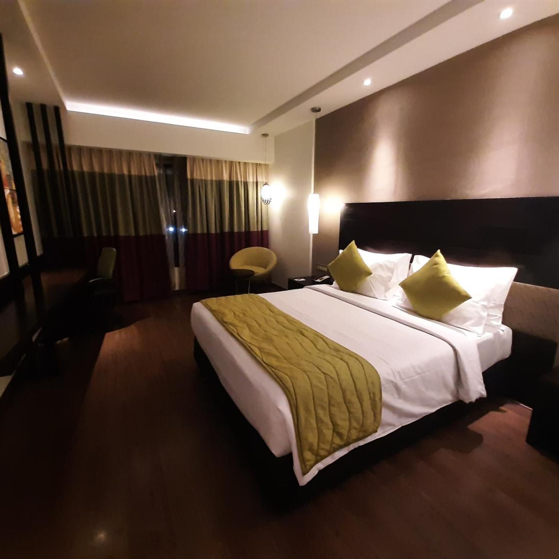 A hotel room with a large bed, a chair, a desk, and a window with curtains.