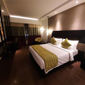 Une chambre d’hôtel avec un grand lit, une chaise, un bureau et une fenêtre avec des rideaux.