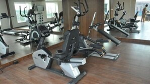 Un gimnasio con diversas máquinas de cardio, un espejo grande y suelo de madera.
