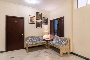 A room with two wooden sofas, a small table with a lamp, and a door with a sign. - Hotel Sarovar (Udaipur)