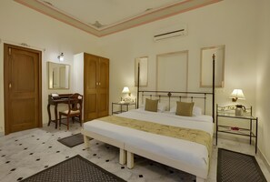 A hotel room with a large bed, bedside tables with lamps, a desk with a chair, and a wardrobe. - Ram Pratap Palace (Udaipur)