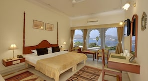 A hotel room with a large bed, a desk, a chair, a TV, and a view of the sea. - Ram Pratap Palace (Udaipur)