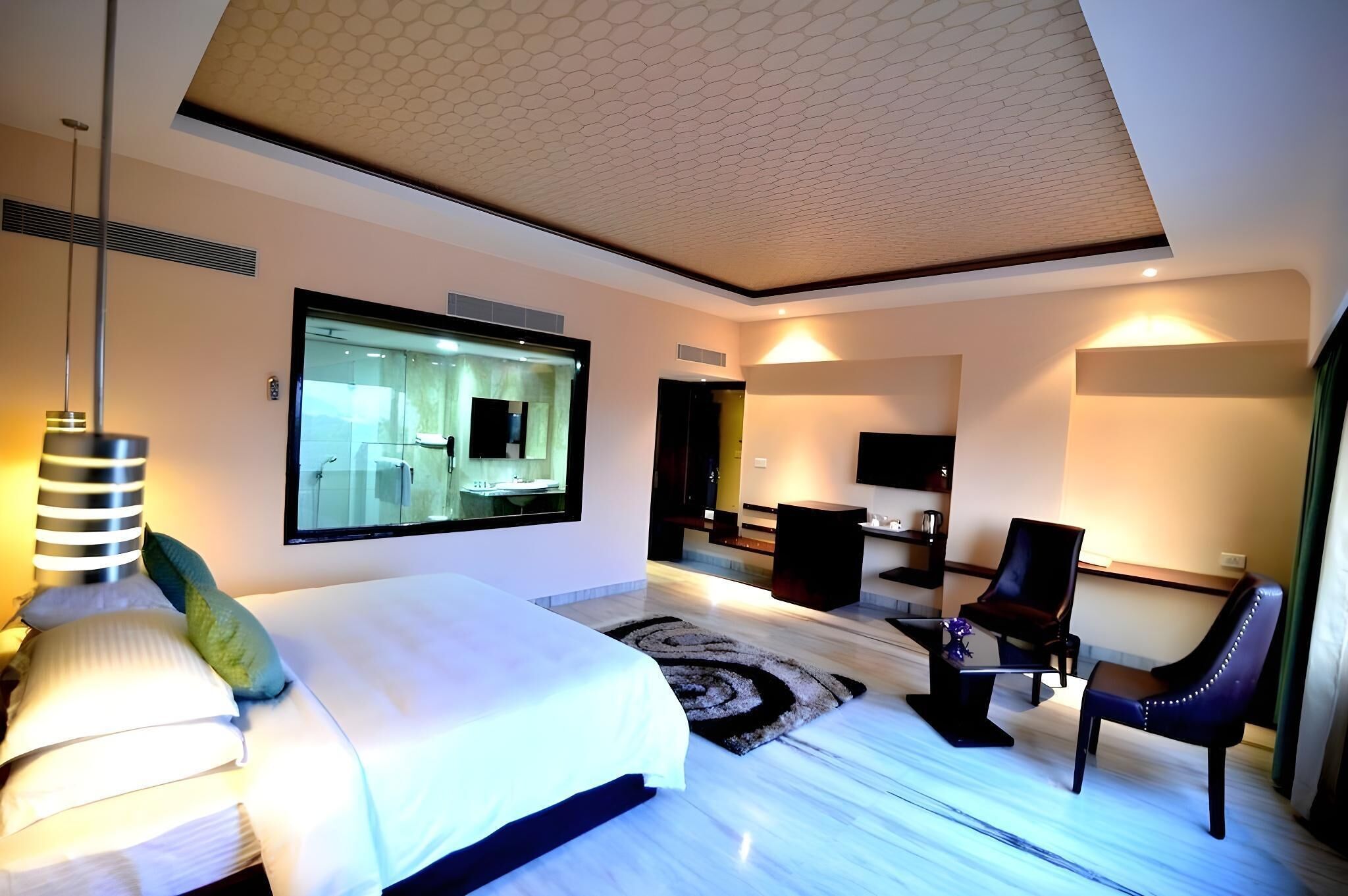 A modern hotel room with a large bed, a sitting area with a chair, a television, and a large mirror.