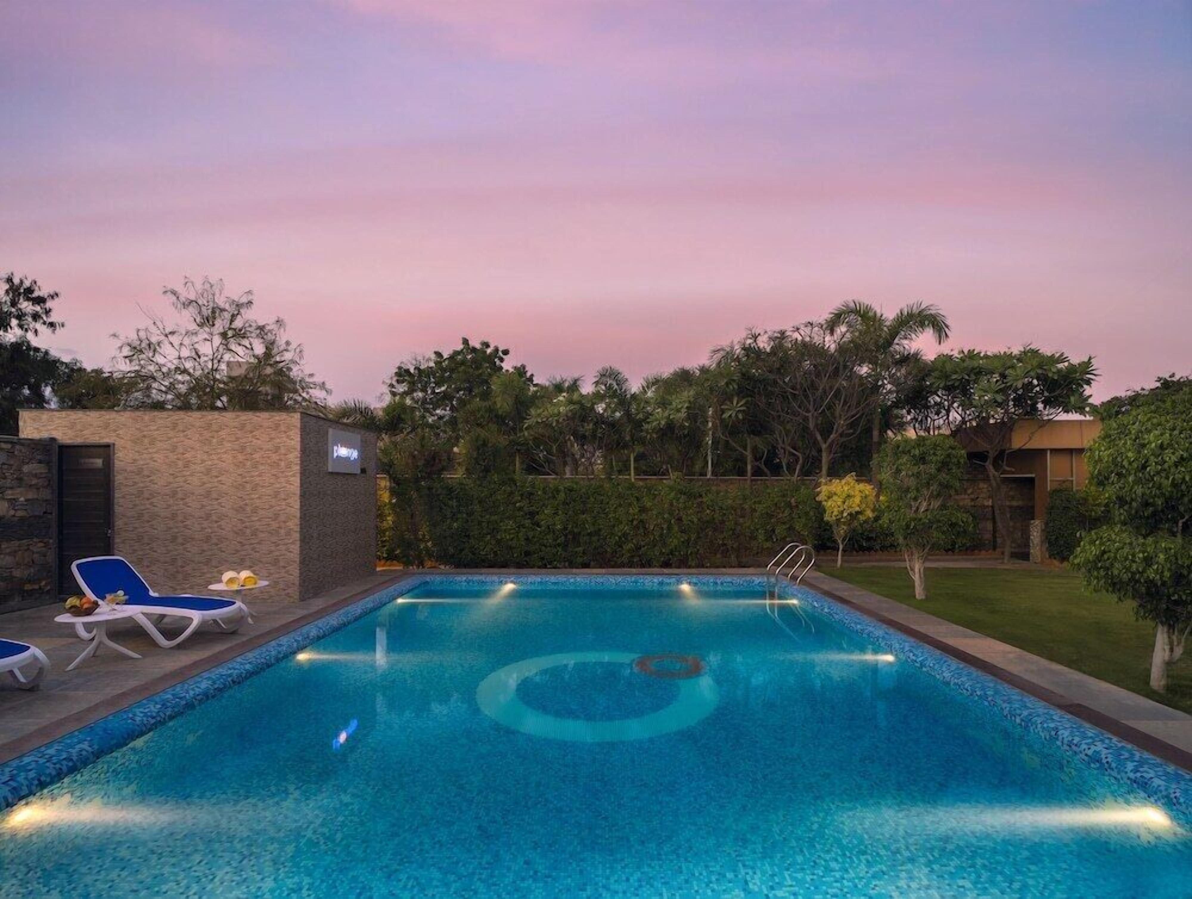 A rectangular swimming pool with a built-in slide, surrounded by lounge chairs and a small table with fruit.