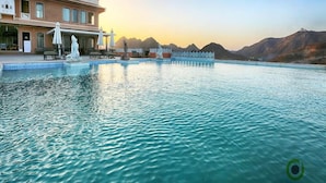 A hotel with a large pool, outdoor seating, and a view of mountains. - Fateh Garh (Udaipur)