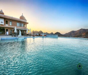 A hotel with a large pool, outdoor seating, and a view of mountains. - Fateh Garh (Udaipur)