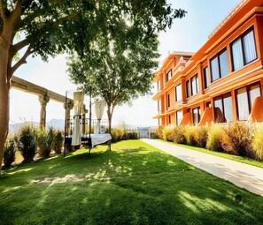 A well-maintained outdoor area with a lawn, a pergola with a table, and a modern building with large windows. - Fateh Garh (Udaipur)