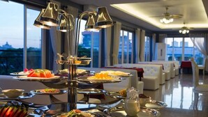 Un buffet composé de plusieurs plateaux de nourriture, d’un espace central pour servir les plats et d’un coin salon avec des canapés blancs.