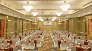 Un salón de conferencias con filas de mesas y sillas, candelabros y un cartel en la pared.