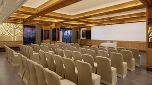 A conference room with rows of beige chairs, wooden beams on the ceiling, and a projection screen. - E Square the Fern Pune (Pune)