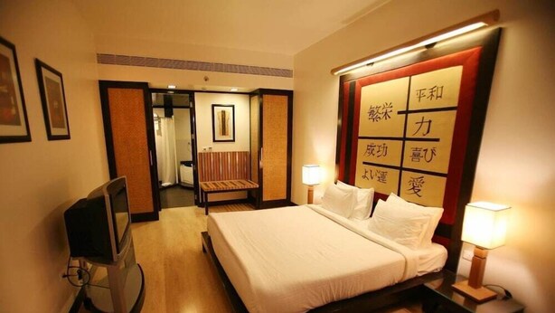 A hotel room with a bed, bedside lamps, a television, and a wall with Japanese characters. - E Square the Fern Pune (Pune)