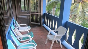 A covered outdoor seating area with rows of chairs and a single chair facing a blue wall with decorative cutouts. - Raina Beach Apartments (Rarotonga)