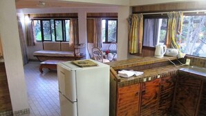 A compact kitchen with a refrigerator, wooden cabinets, and a bench in the background. - Raina Beach Apartments (Rarotonga)
