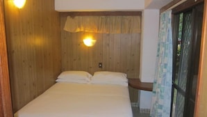 A single bed in a room with wooden walls and a ceiling fan. - Raina Beach Apartments (Rarotonga)
