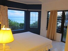 A bedroom with a bed, a lamp, and a view of the sea through large windows.