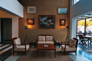 A lobby with a sofa, chairs, a coffee table, framed artwork, and a view of the outdoors. - Eighth Bastion Fort Kochi - A CGH Earth Experience (Kochi)