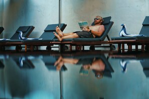 A person lying on a sun lounger reading a book.