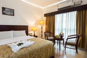 A hotel room with a large bed, two chairs, a small table with flowers, and a window with curtains.