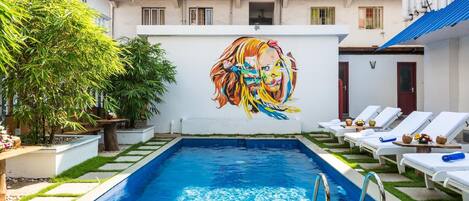 Una piscina con sillas de descanso y un mural en la pared.