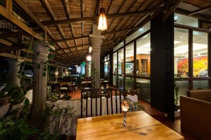 Un comedor interior con vigas de madera, luces colgantes y plantas en macetas.