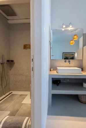 A modern bathroom with a large mirror, a sink, and a shower area. - La Stella Hotel (Mykonos)