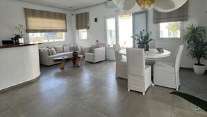 A modern living room with a dining area, featuring a sofa set, a coffee table, and a dining table with chairs. - Anna Maria Mykonos Hotel (Mykonos)