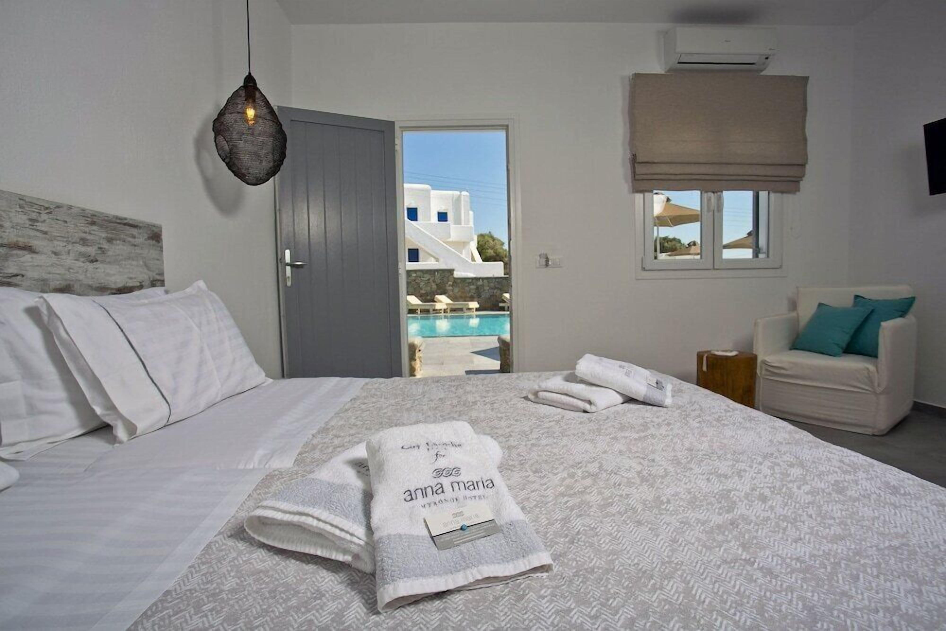 A hotel room with a bed, a view of the pool, a chair, and a TV.