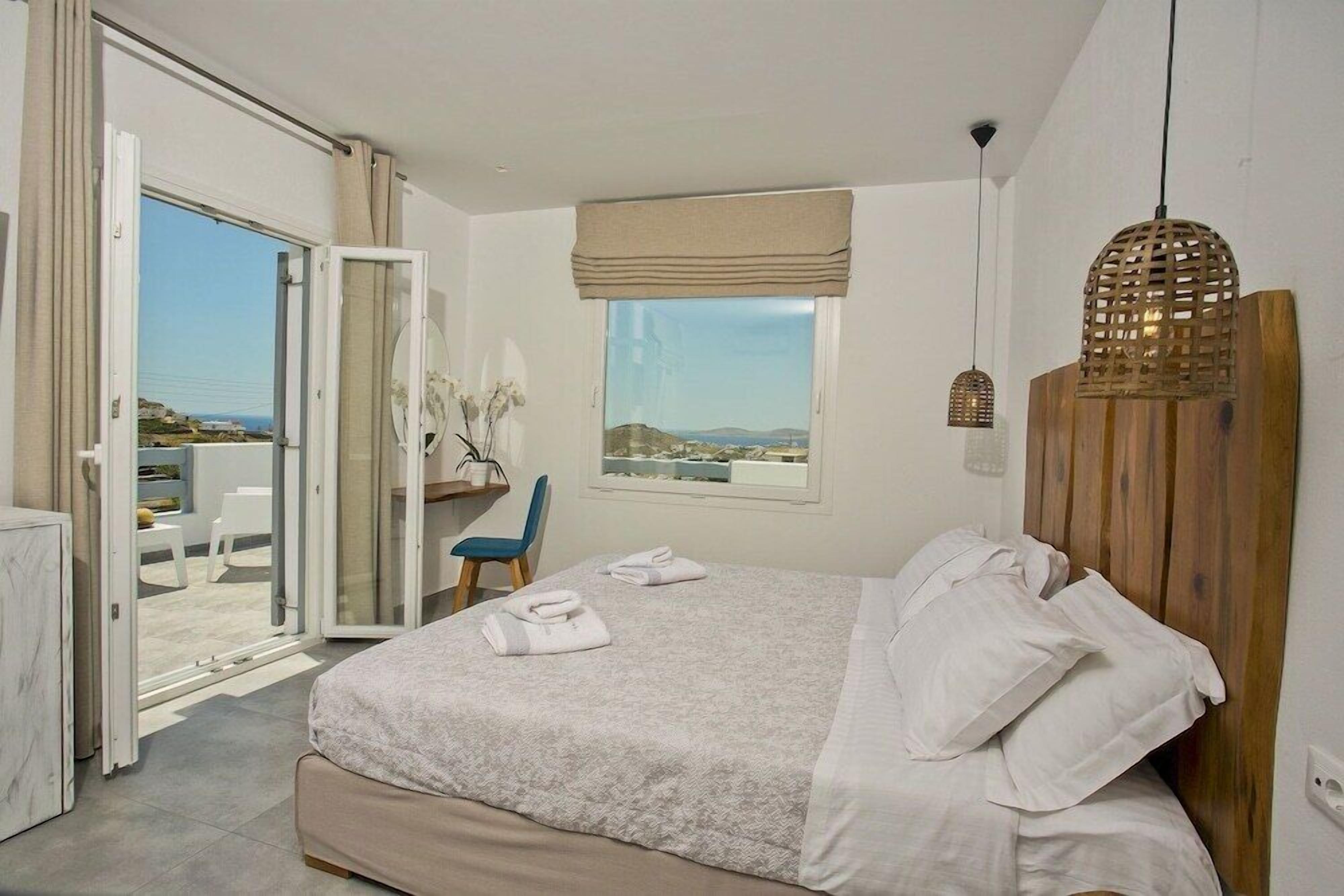 A bedroom with a bed, a desk, and a view of the sea.