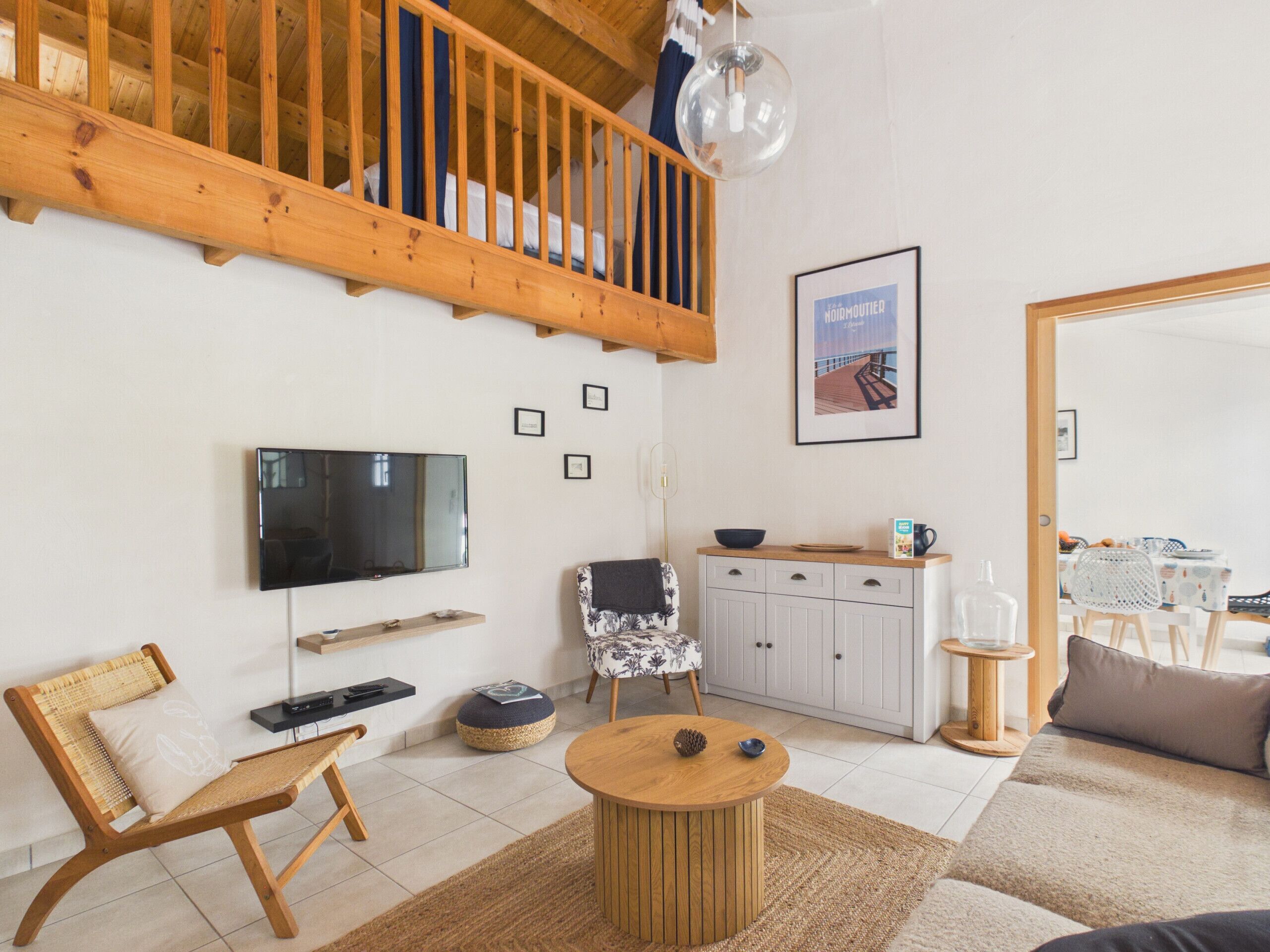 Ein modernes Wohnzimmer mit einer Holztreppe, einem Flachbildfernseher, einem Essbereich mit Tisch und Stühlen sowie einer Küchenzeile mit Schränken und einer Pendelleuchte.