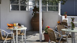 An outdoor patio with wicker chairs and tables, a large vase with flowers, and a stone wall. - Asteri Hotel Ornos (Mykonos)