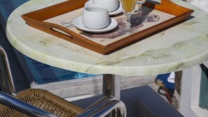 A poolside table with a tray of breakfast items, including cups, a glass of orange juice, and a glass of water. - Asteri Hotel Ornos (Mykonos)
