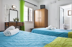 Un dormitorio con dos camas, un armario de madera, un escritorio con espejo y un baño visible a través de una puerta abierta.