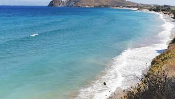 A coastal landscape with a clear view of the sea, a sandy beach, and a prominent hill in the background.