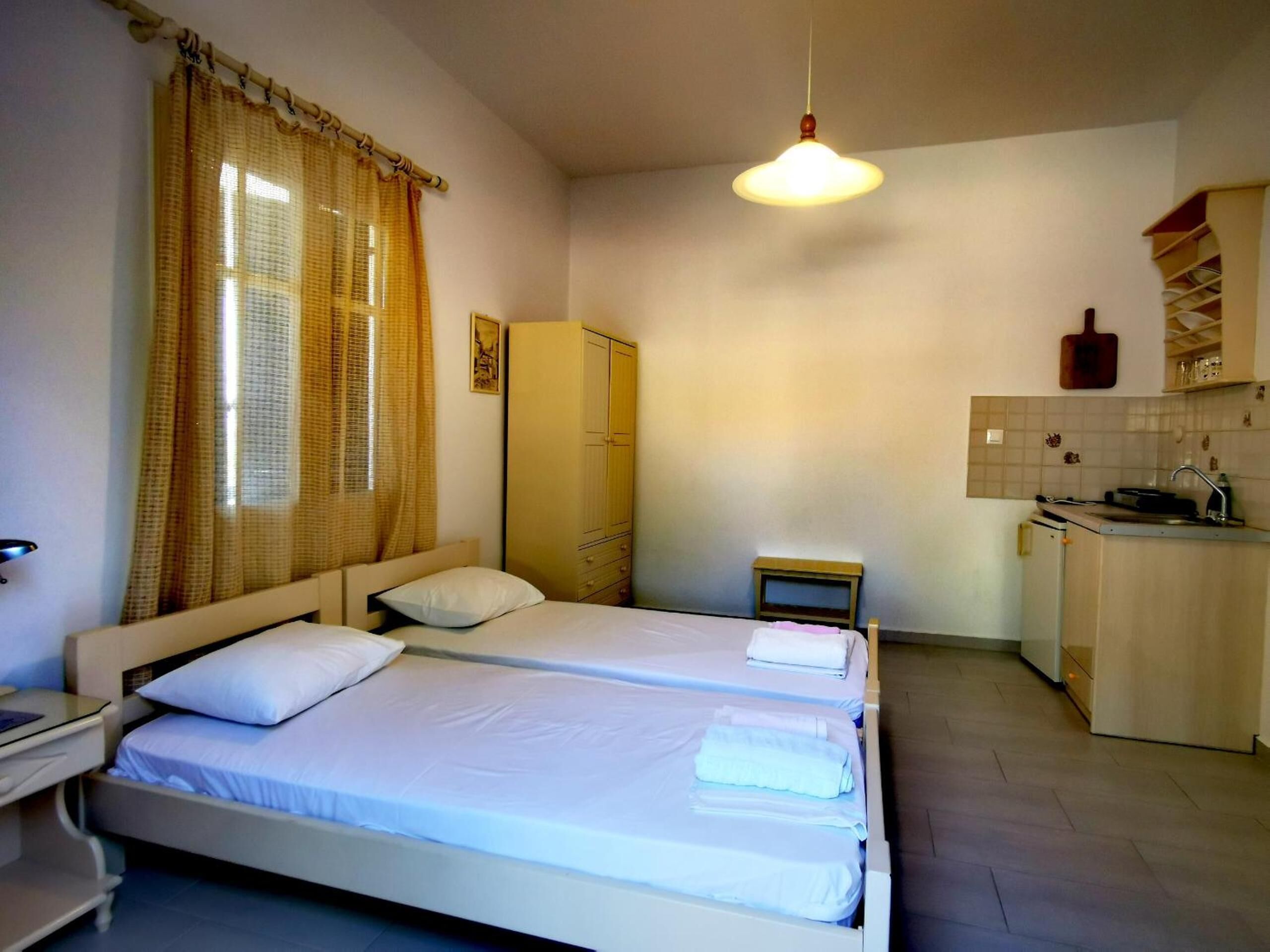Une chambre avec deux lits, une petite table de chevet, une armoire et un coin cuisine.